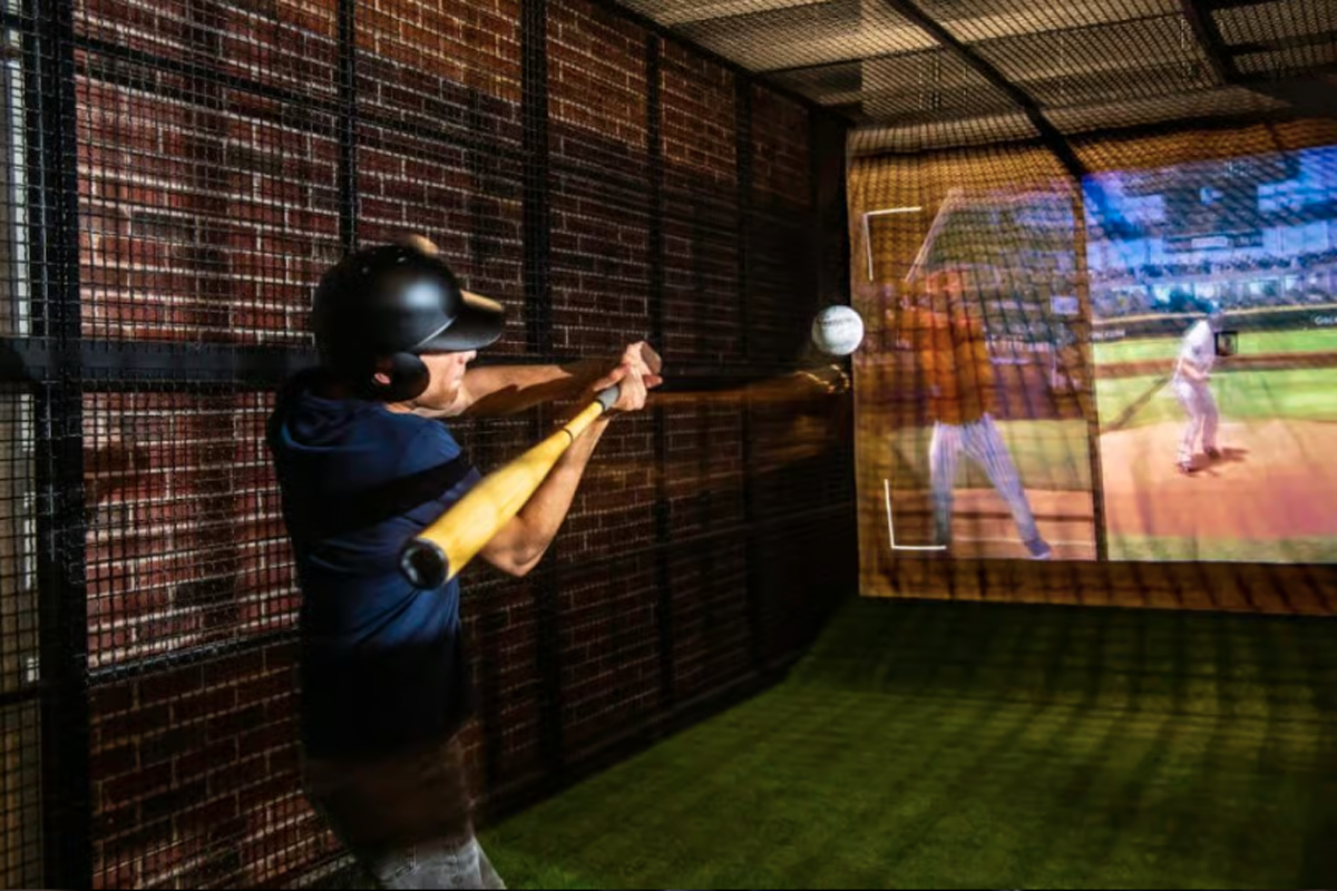 A young man swinging a bat at a baseball in a Batbox baseball simulator.
